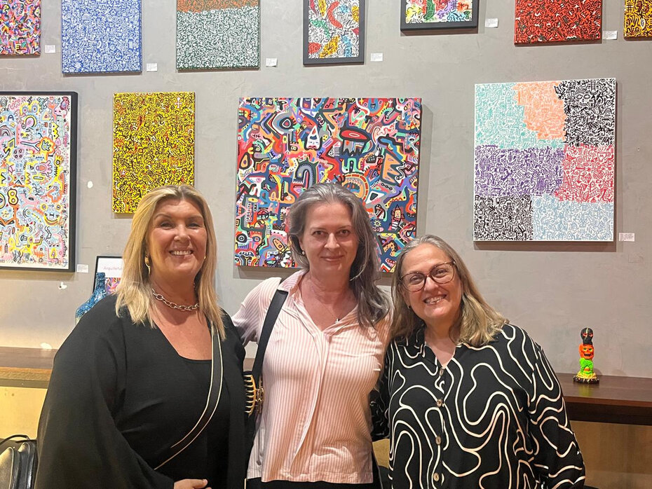 Katia Vreenegor, Carla Baldissera e Roseane Coelho tendo ao fundo as obras de Tiago Gregório (Foto: Divulgação)